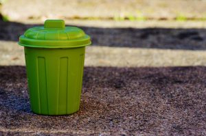A green garbage bucket on the ground, to help you clean your apartment with ease.
