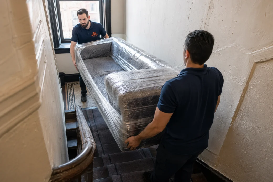 Big Apple Moving crew carrying a wrapped sofa down a New York walk-up stairwell